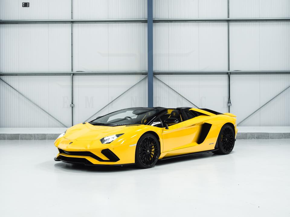 A yellow sports car with black wheels is parked indoors against a light-colored industrial backdrop, available for hire.