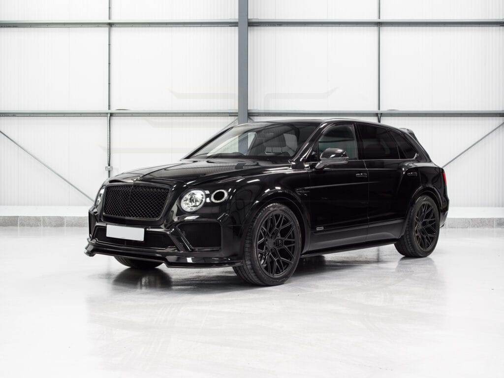 Black luxury SUV available for hire, parked in a clean, brightly lit industrial garage with gray walls and a metal framework.