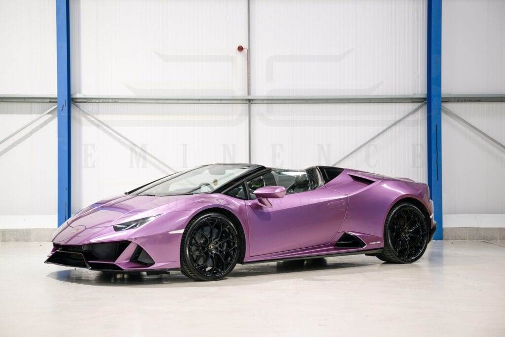 A purple convertible sports car with black wheels is parked indoors against a white and blue wall background, ready for hire.
