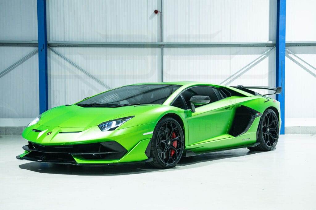 A bright green sports car with a sleek design and black accents is parked in a well-lit, industrial-style garage, waiting for someone to hire it for an exhilarating drive.