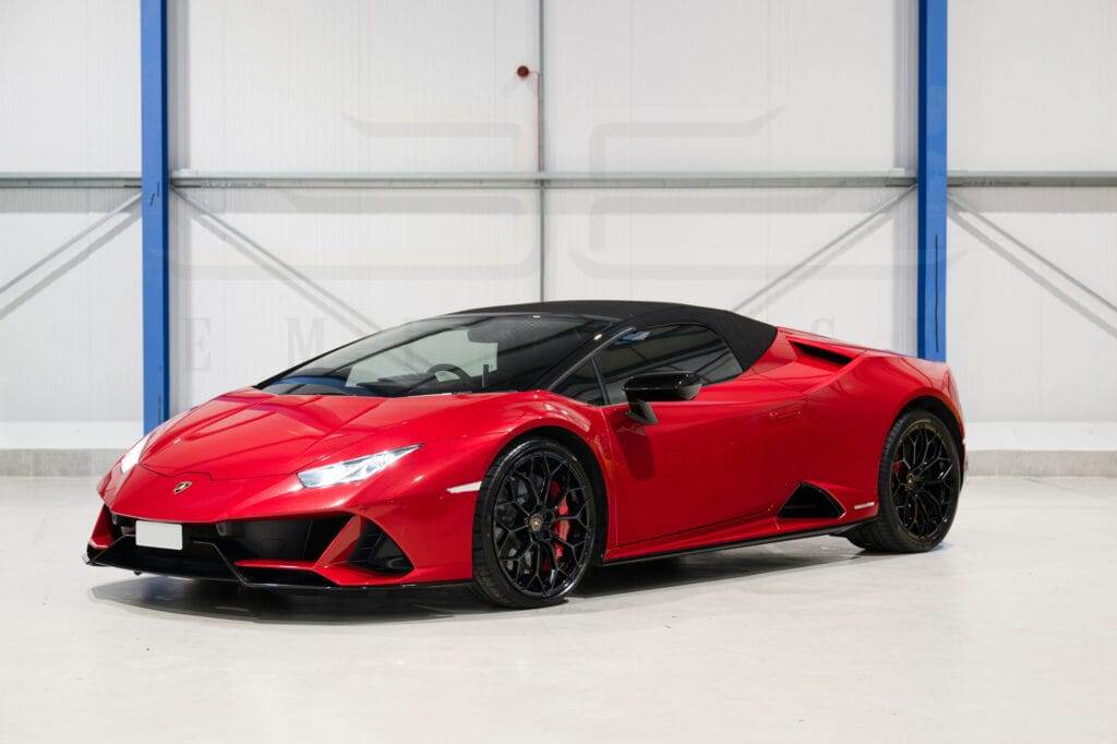 A red convertible sports car with black accents, available for hire, is parked indoors against a striking white and blue wall.