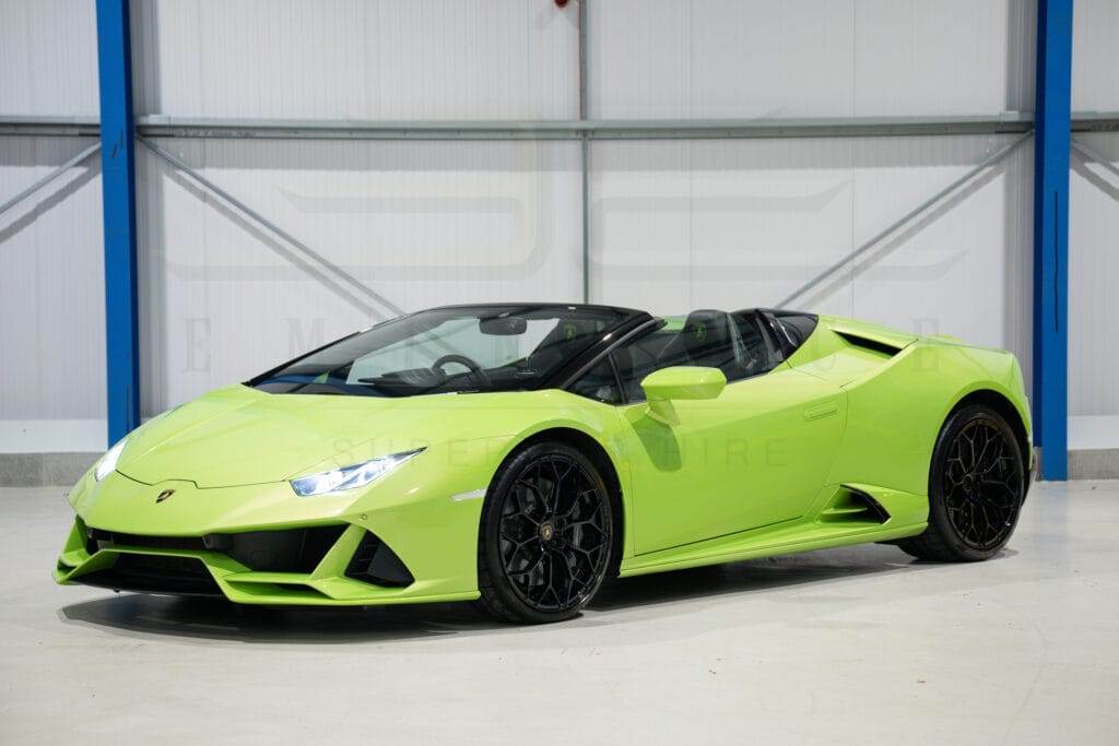 A bright green convertible sports car with black wheels is parked in a clean, indoor facility with a blue and gray color scheme, available for hire.