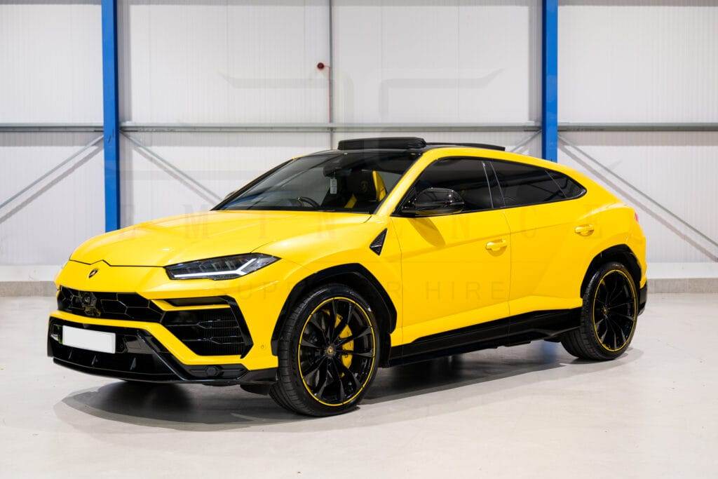 A bright yellow luxury SUV available for hire is parked indoors on a clean, white floor next to a blue and white wall.