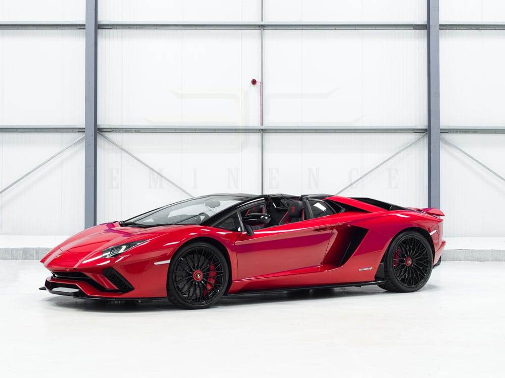 A red convertible sports car is parked in a large, modern, white garage. The car features sleek lines and black wheels, available for hire.