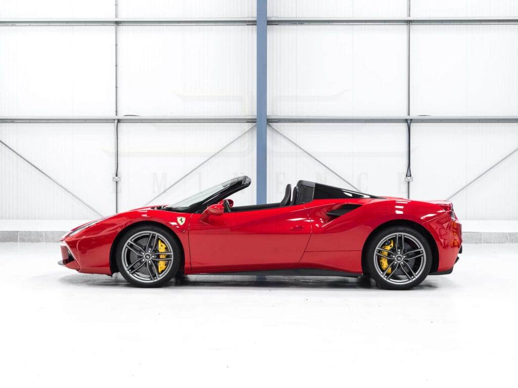 Side view of a red convertible sports car available for hire in an indoor garage with a white background.