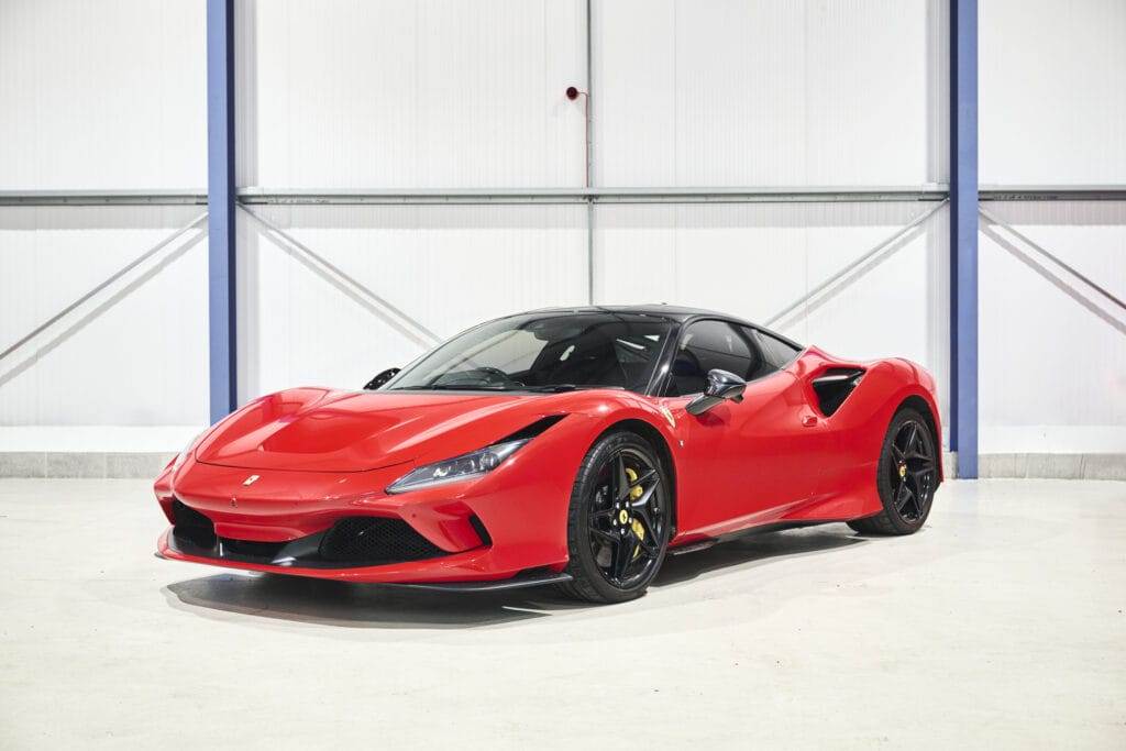 A red sports car with a black roof, available for hire, is parked indoors on a white floor, positioned at an angle showing the front and side profile.
